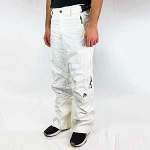 Y2K Women's Deadstock Vintage Nike ACG Cargo Ski Pants in white with Nike ACG branding. Storm Fit 5 technology to keep you comfortable and dry in rain, sleet, and snow. Fleeced inner layer. Zip pockets. Boot gaiters. Belt loops for belt adjustment. - Materials: Body: Nylon Fill: Polyester