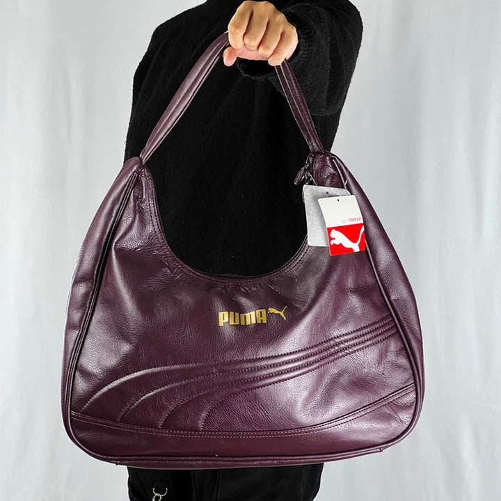 Your sports outfit will not be as attractive without the Puma Sister Handbag. Dark purple in colour, it has the Puma logo printed in gold on the front. It has a roomy compartment with three inner pockets. Materials: 100% polyurethane Colour: Dark purple Brand New with Tags