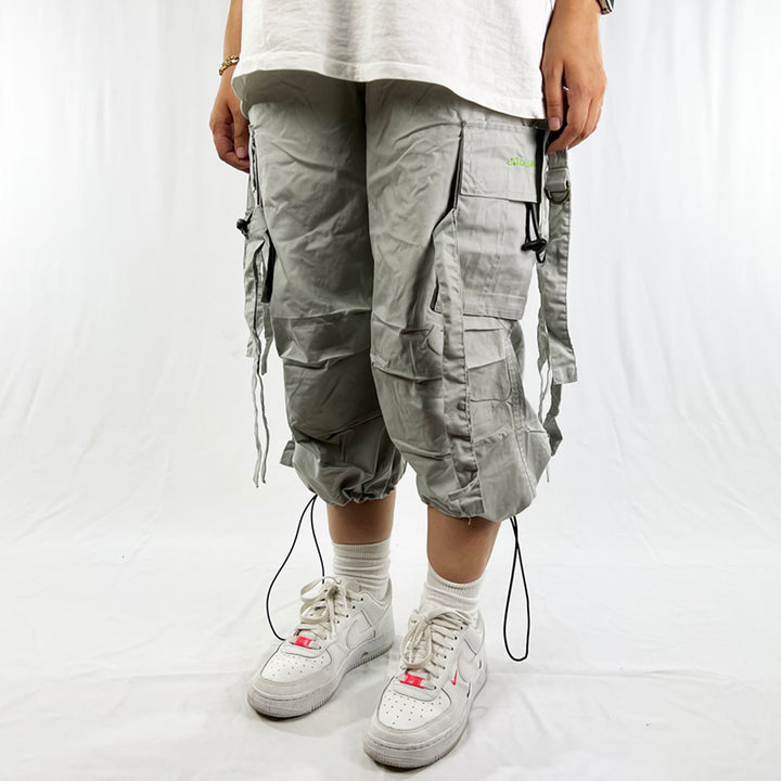 Y2K Women's Deadstock Vintage Criminal Damage Drome cargo shorts in grey with Criminal Damage branding. Lattice style parachute cargos. Adjustable drawstring to waist. Pockets to side. Adjustable cord to hem. Material: Polyester/Cotton Colour: Grey Brand New with Tags