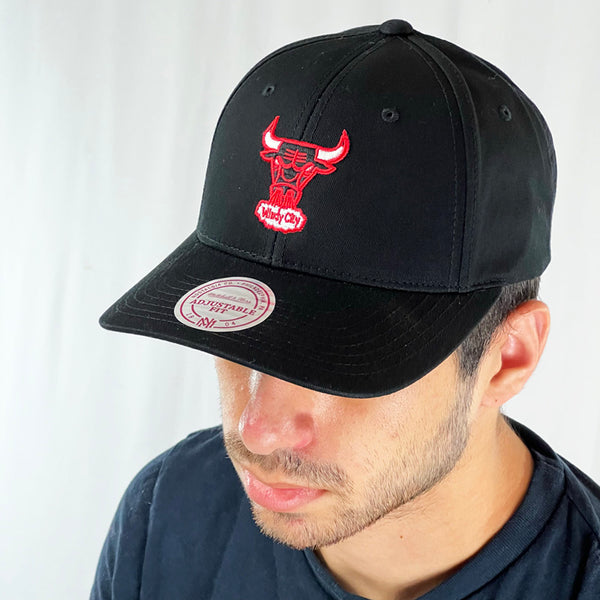 Support the NBA Chicago Bulls basketball team with this low profile snapback cap. Finished in black and paired with a curved visor, the fitted crow features the iconic Chicago bulls logo with the windy city spellout fully fitted for your complete comfort in a range of sizes. Mitchell & Ness embroidery to rear Colour: Black Brand New with Tags - Size on Tag: One Size