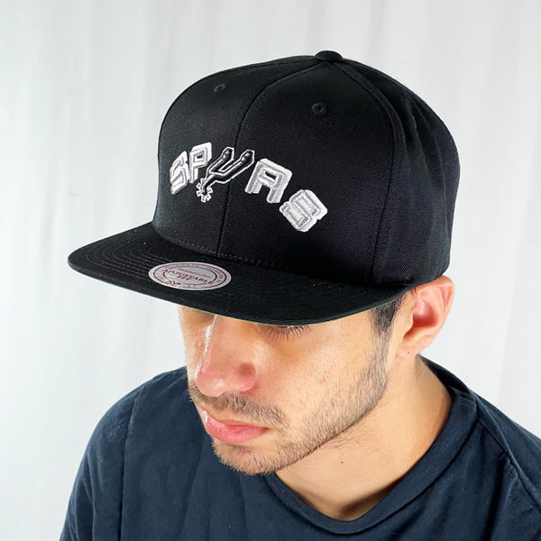 Support the NBA San Antonio Spurs basketball team with this low profile snapback cap. Crafted with a high structured crown finished in black and paired with a flat visor, the fitted crow features the iconic Spurs spellout logo fully fitted for your complete comfort in a range of sizes. Mitchell & Ness embroidery to rear Colour: Black Brand New with Tags - Size on Tag: One Size