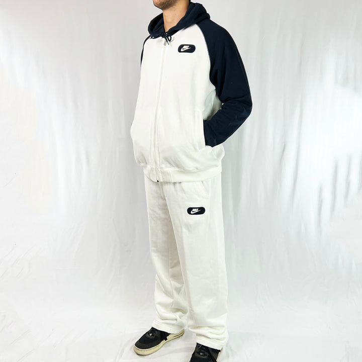 2006 Deadstock Vintage Nike Tracktown tracksuit set in white and navy. Full zip closure and pockets available on hoodie. The matching pants have an adjustable drawstring for a customised wear, as well as side pockets to keep your essentials. Nike branding detailed on hoodie and joggers. Small mark may be washable as shown in image. Material: 80% Cotton 20% Polyester Colour: White & Navy  Brand New with Tags  Size on Tag: Medium
