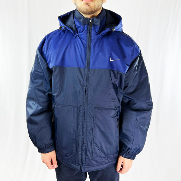 90s Deadstock Vintage Nike Spellout Jacket in Navy Blue. Embroidered Nike Swoosh to chest and Nike spellout to back. Adjustable cord on hood. Removeable zipped hood. Zip pockets to side and inner layer. Adjustable cord to waist. Zip closure Jacket. - Materials: Nylon Fill: Polyester