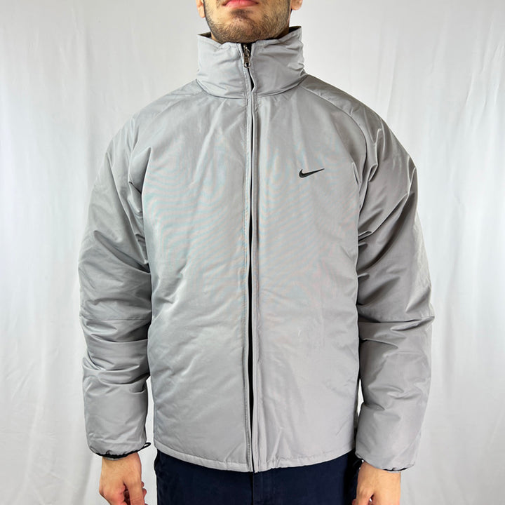 2003 Deadstock Vintage Nike Sporting Excellence Puffer Jacket in Grey. Embroidered Nike swoosh logo to chest. Zip pockets to front. Zip closure to jacket. Sporting Excellence Since 1971 spellout to back. - Colour: Grey Brand New With Tags - Size on Tag: Small Measurements: Pit to Pit: 21 Inches Length: 26.5 Inches