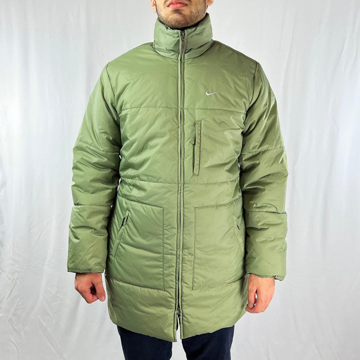 Y2K Women's Deadstock Vintage Nike Swoosh Puffer Jacket in Green. Embroidered Nike logo to chest. Long length jacket. Zip closure. Zip pockets to front. Hood hidden in hood compartment behind neck for rainy days. Fleeced inner layer. - Material: Body: Nylon Lining: Polyester Fill: Polyester