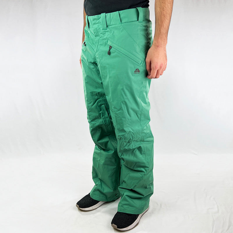 Y2K Women's Deadstock Vintage Nike ACG Cargo Ski Pants in green with Nike ACG branding. Storm-Fit technology. Thermore light insulation fleeced inner layer. Zip pockets to sides and inner thigh. Boot gaiters. Belt loops for belt adjustment. - Materials:  Body: Nylon Fill: Polyester
