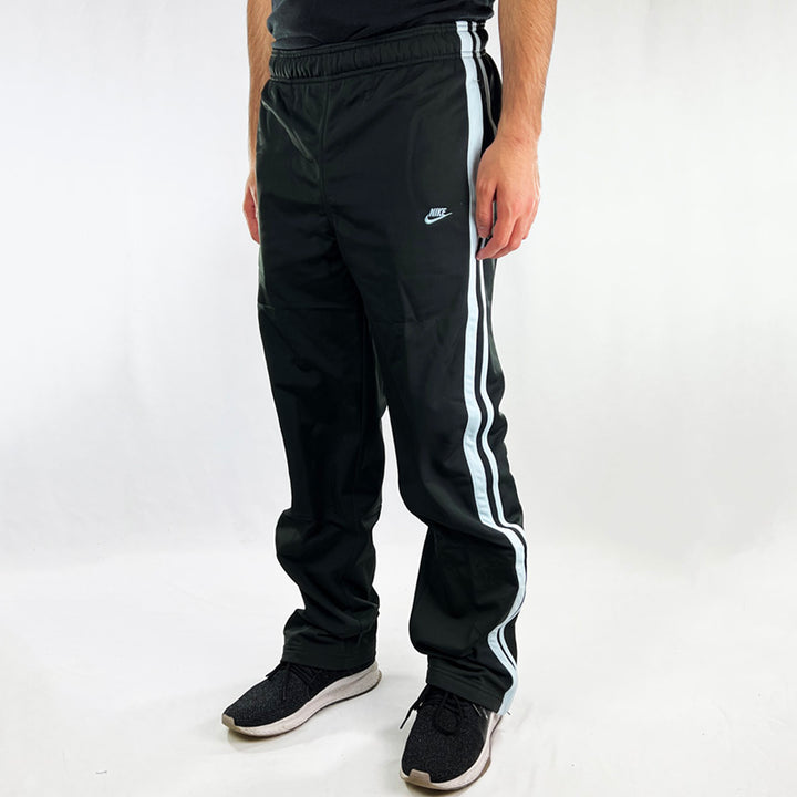 Y2K Deadstock Vintage Nike joggers in black. Nike spellout logo to front with blue detailing. Pockets to sides. Adjustable drawstrings to waist. Zip closure to hem. - Materials: 100% Polyester - Colour: Black Brand New with Tags  - Size on Tag: Small Length: 41.5 Inches Inseam: 31 Inches Waist: Adjustable drawstring