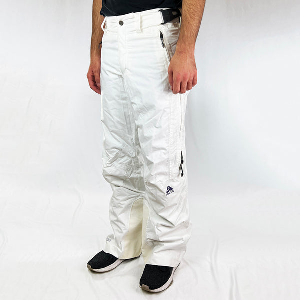 Y2K Women's Deadstock Vintage Nike ACG Cargo Ski Pants in white with Nike ACG branding. Storm Fit 5 technology to keep you comfortable and dry in rain, sleet, and snow. Fleeced inner layer. Zip pockets. Boot gaiters. Belt loops for belt adjustment. - Materials:  Body: Nylon Fill: Polyester