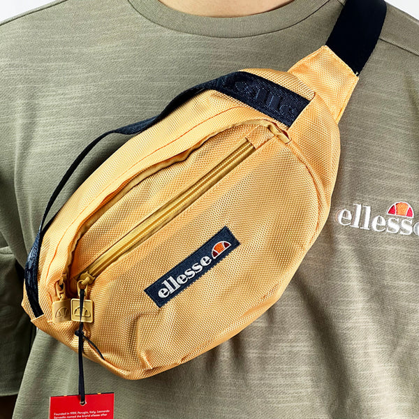 The Sanri Bumbag. Walk round in style this season with the ellesse Sanri bumbag. The perfect way to style up any outfit, this bumbag has a waist strap and a carry handle, alongside a drop sleeve on the back. With two compartments with zip fastenings, the bag is complete with the classic ellesse embroidered logo on the front. Colour: Sak Yellow