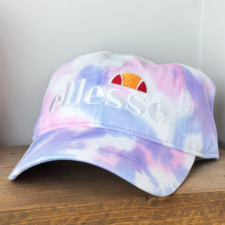 Deadstock Ellesse Ragusa cap in tie dye. Curved visor. Ellesse spellout to front. Adjustable strapback. Materials: 100% Cotton Colour: Tie Dye Brand New with Tags - Size on Tag: One Size