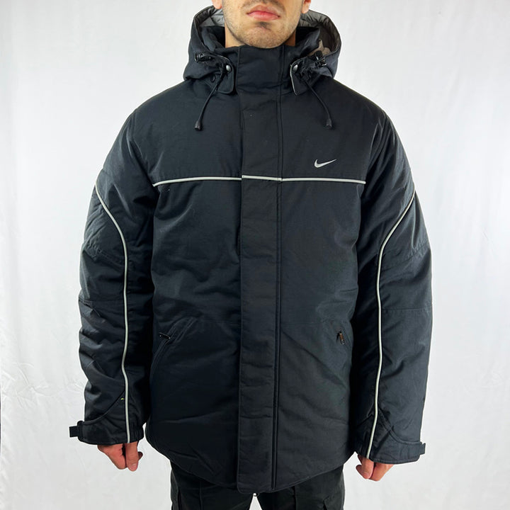 Y2K Deadstock Vintage Nike swoosh puffer jacket in black. Embroidered Nike swoosh to chest. Zip pockets to front. Zip closure to jacket. Inner pocket. Removeable hood. Adjustable cord to hood. Padded. - Materials: Body: Nylon Fill: Polyester - Colour: Black Brand New with Tags - Size on Tag: Medium Measurements: Pit to Pit: 22 Inches Length: 30.5 Inches