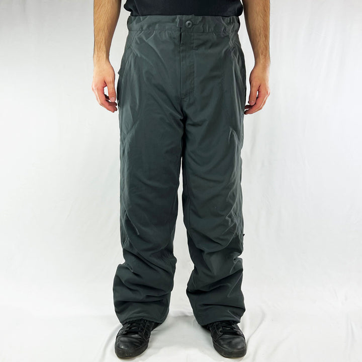 Y2K Deadstock Vintage Nike utility cargo trousers in grey with Nike branding. Padded inner layer. Velcro closure pockets. Belt loops and drawstring for waist adjustment. Zip closure to hem. - Materials: Polyester - Colour: Grey Brand New with Tags - Size on Tag: Large Measurements: Inseam: 32.5 Inches Waist: GB 34/36