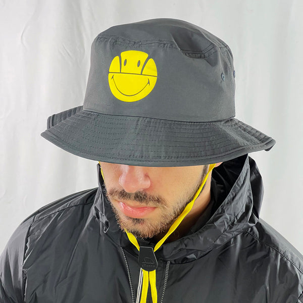 Deadstock Ellesse x Smiley Joyely bucket hat in dark grey. Ellesse spellout to and smiley face on hat. Materials: 100% Polyester Colour: Dark Grey Brand New with Tags - Size on Tag: One Size
